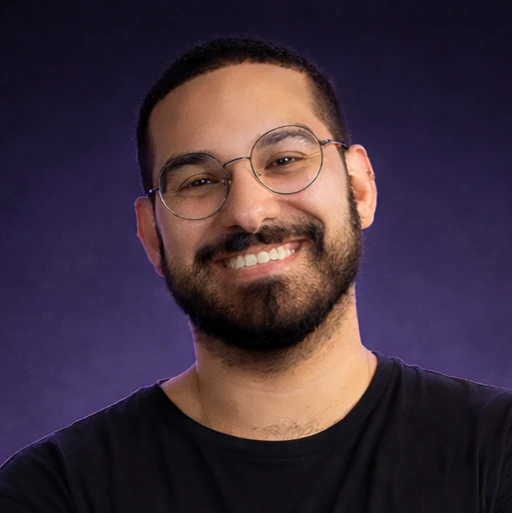 Retrato profissional de João Custódio, com óculos, barba e camisa preta, sorrindo diante de fundo roxo.